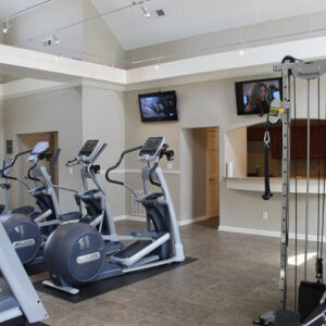 Our gym with treadmills, weight machines, and TV - The Legends Apartments