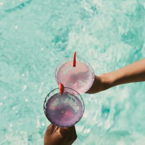 Two people holding drinks above a pool